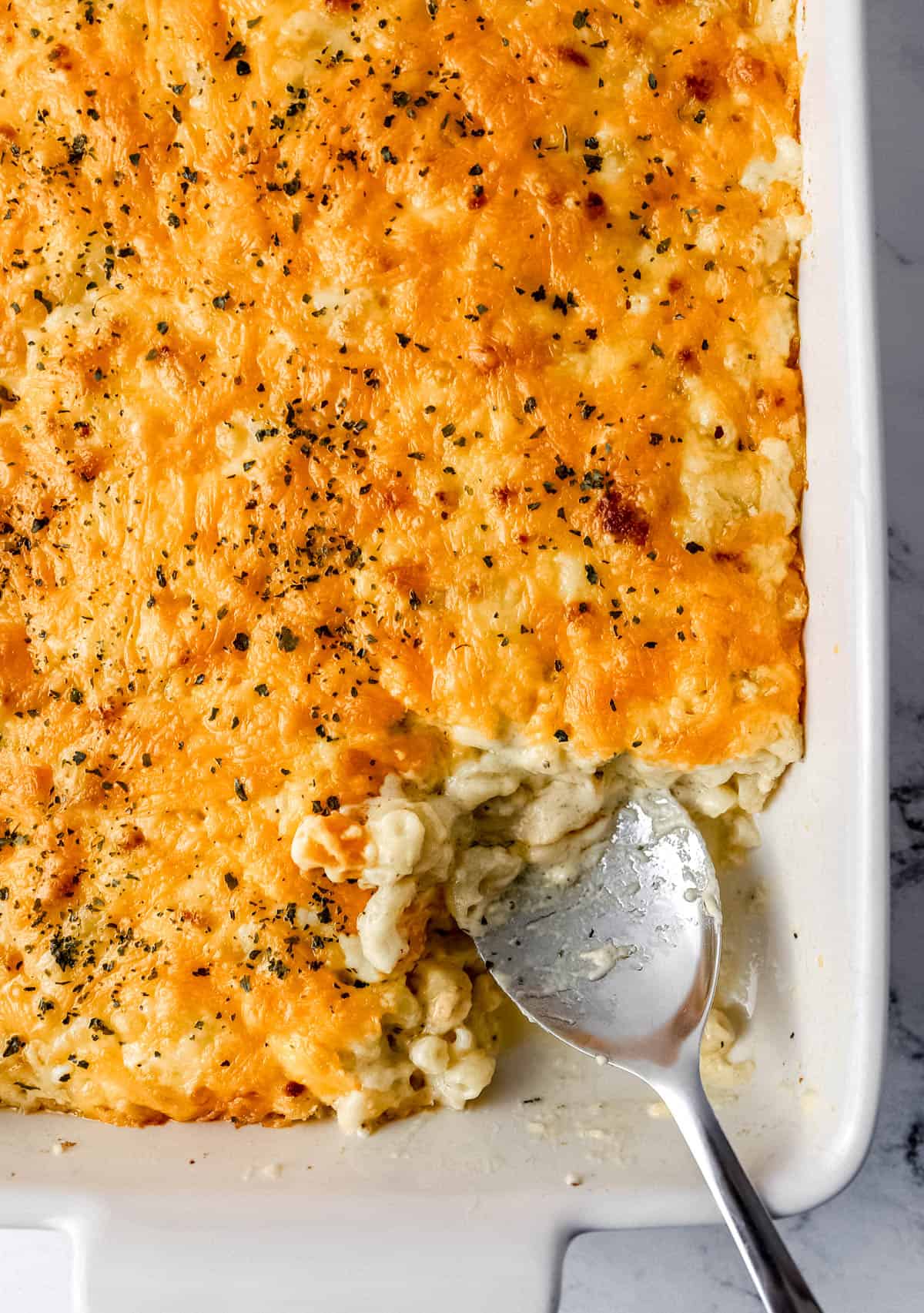 Overhead view of baked mac and cheese in white baking dish with serving spoon in it.