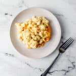 Overhead view of white plate with serving of mac and cheese on it beside a fork.
