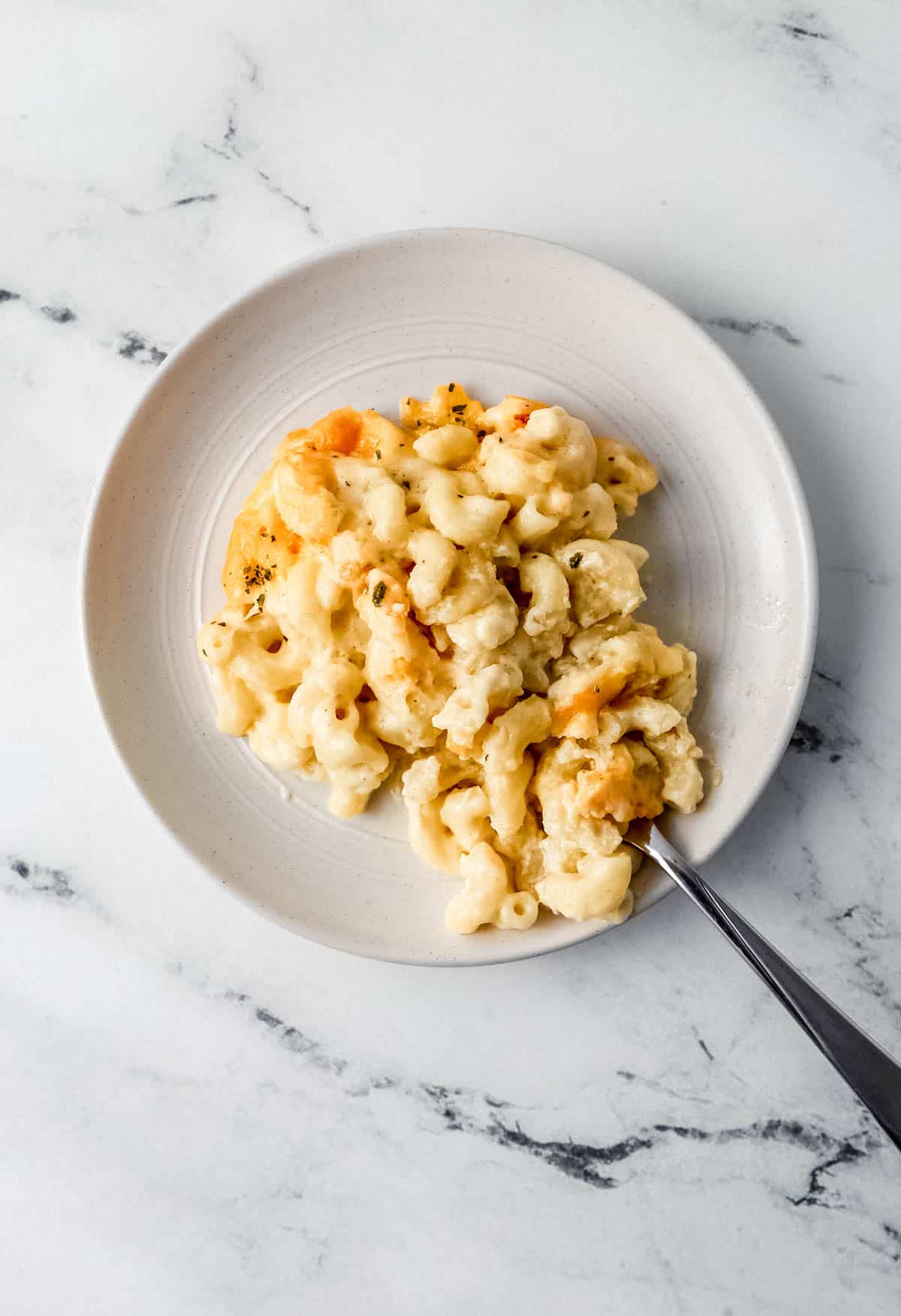 White plate with single serving of mac and cheese on it with a fork in it. 