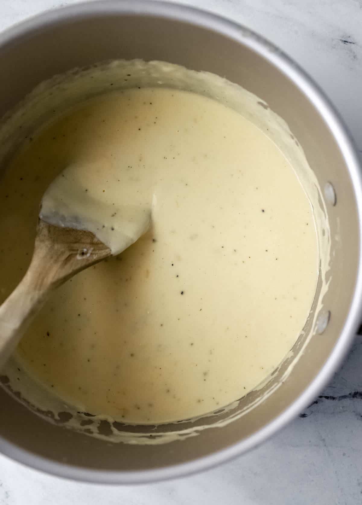 Cheese sauce in stockpot with wooden spoon in it.