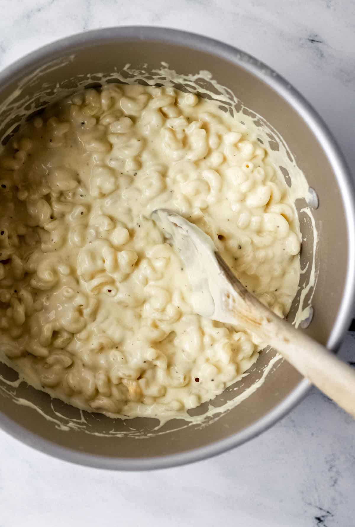 Macaroni added to cheese sauce in stockpot with wooden spoon. 