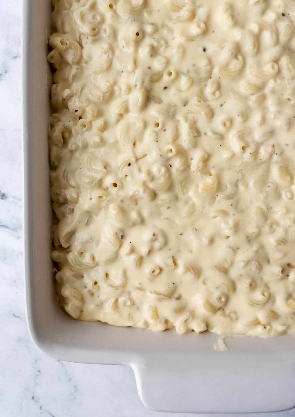 Pasta and sauce added to rectangle baking dish on marble surface. 