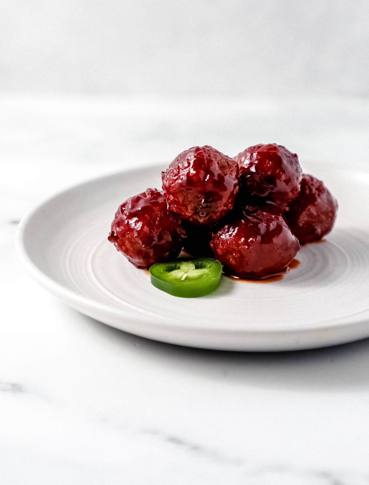 Close up side view of meatballs on white plate with slices jalapenos. 