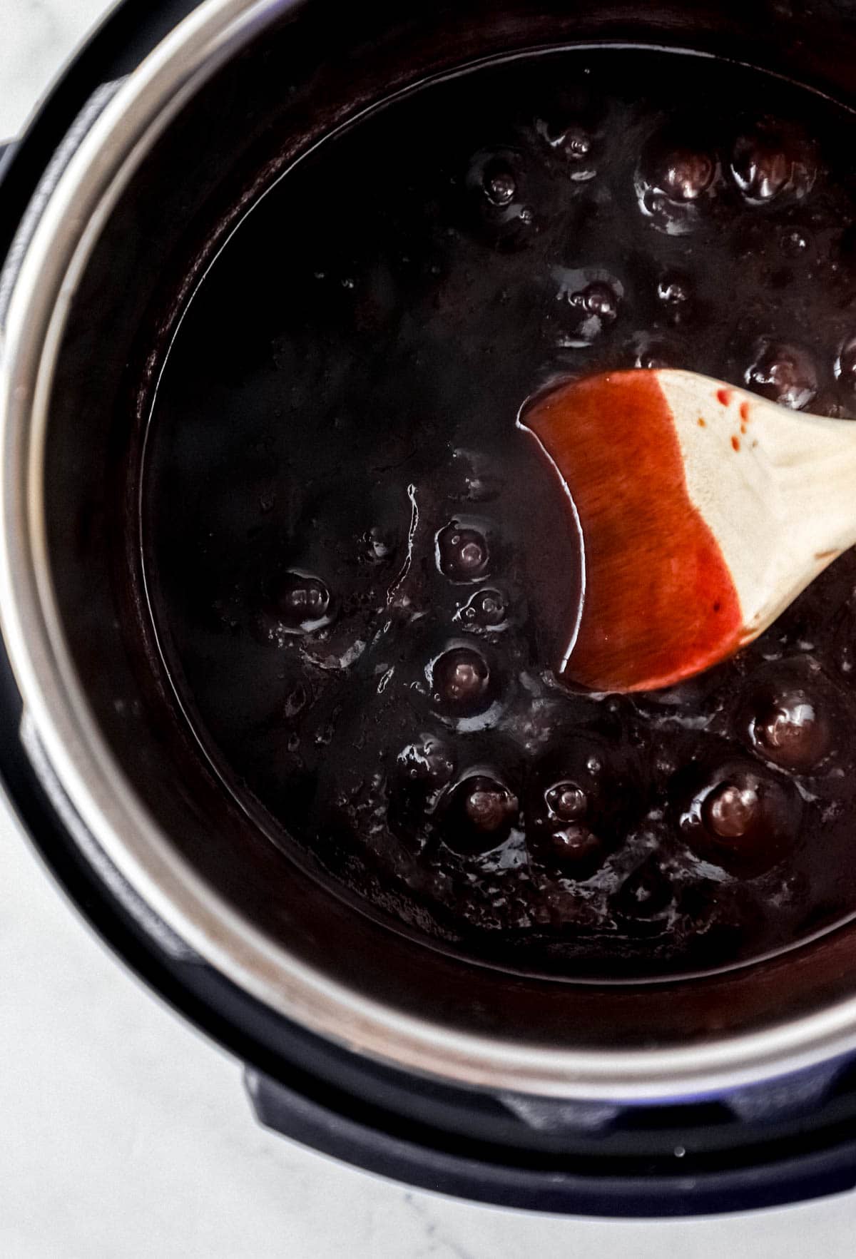 Overhead view of jam and bbq sauce in pressure cooker with a wooden spoon. 