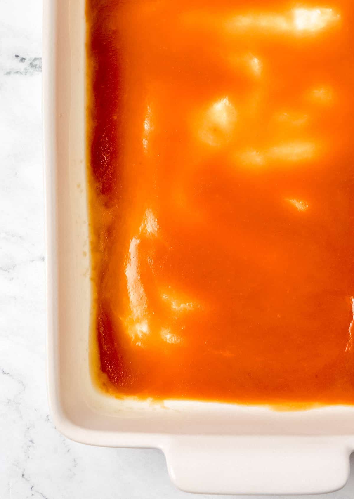 Overhead view of brown sugar and melted butter added into the bottom of a white baking dish. 