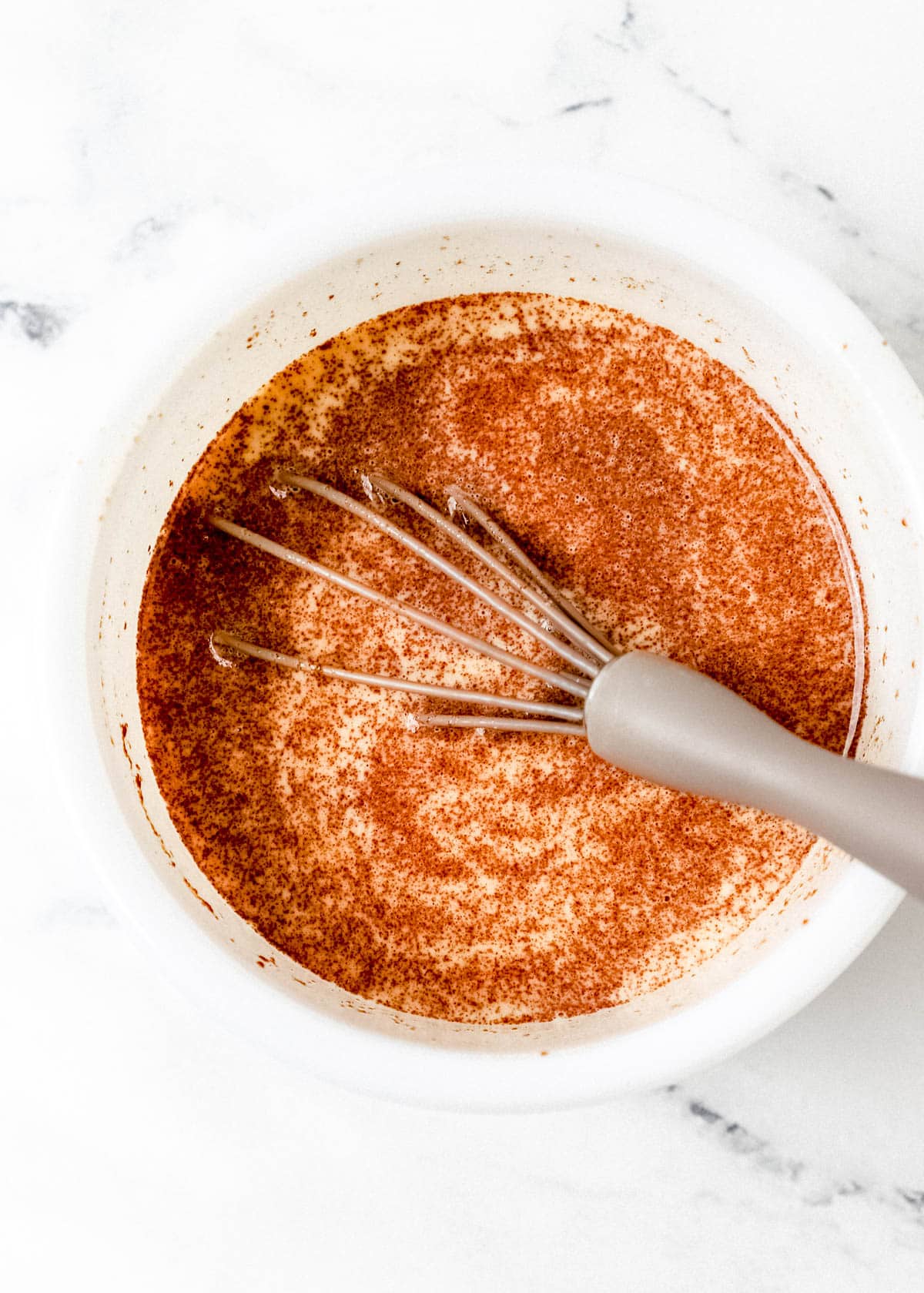 Ingredients to make egg mixture added to white bowl with whisk. 