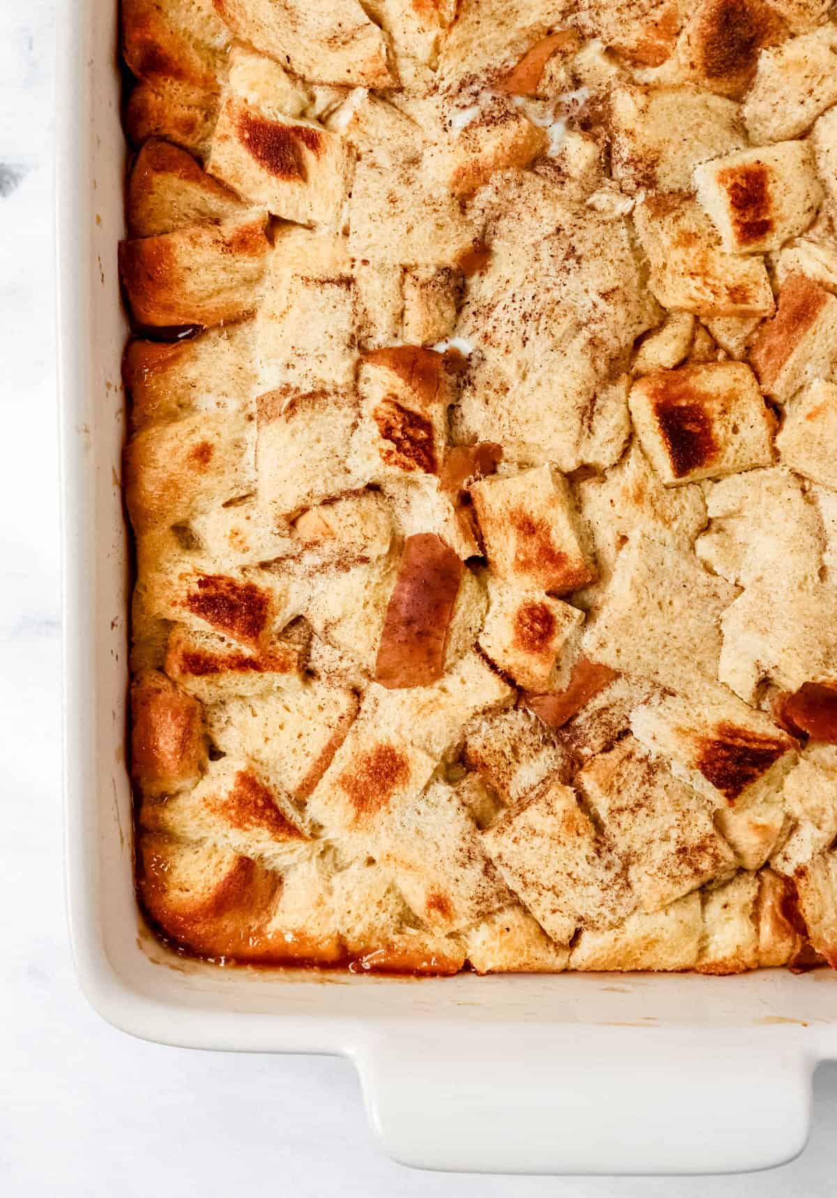 Overhead view of baked french toast in white rectangle baking dish on marble surface. 