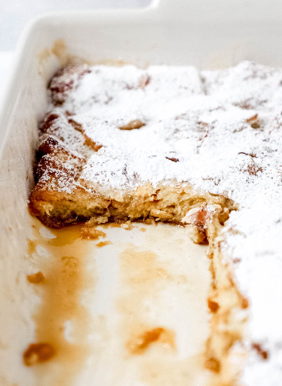 Close up view of french toast in baking dish with pieces taken out of it. 