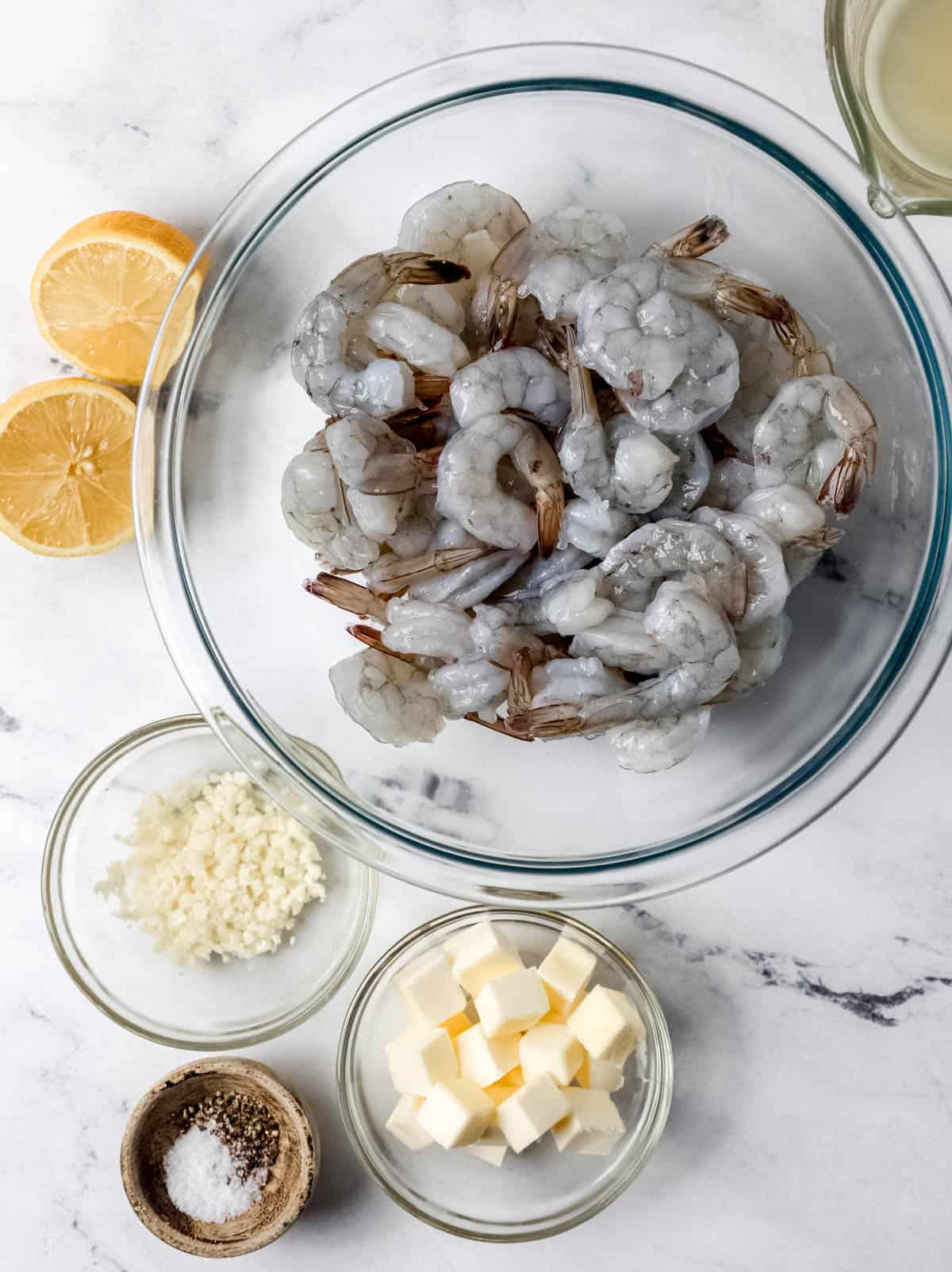 Ingredients needed to make shrimp in separate bowls on marble surface. 