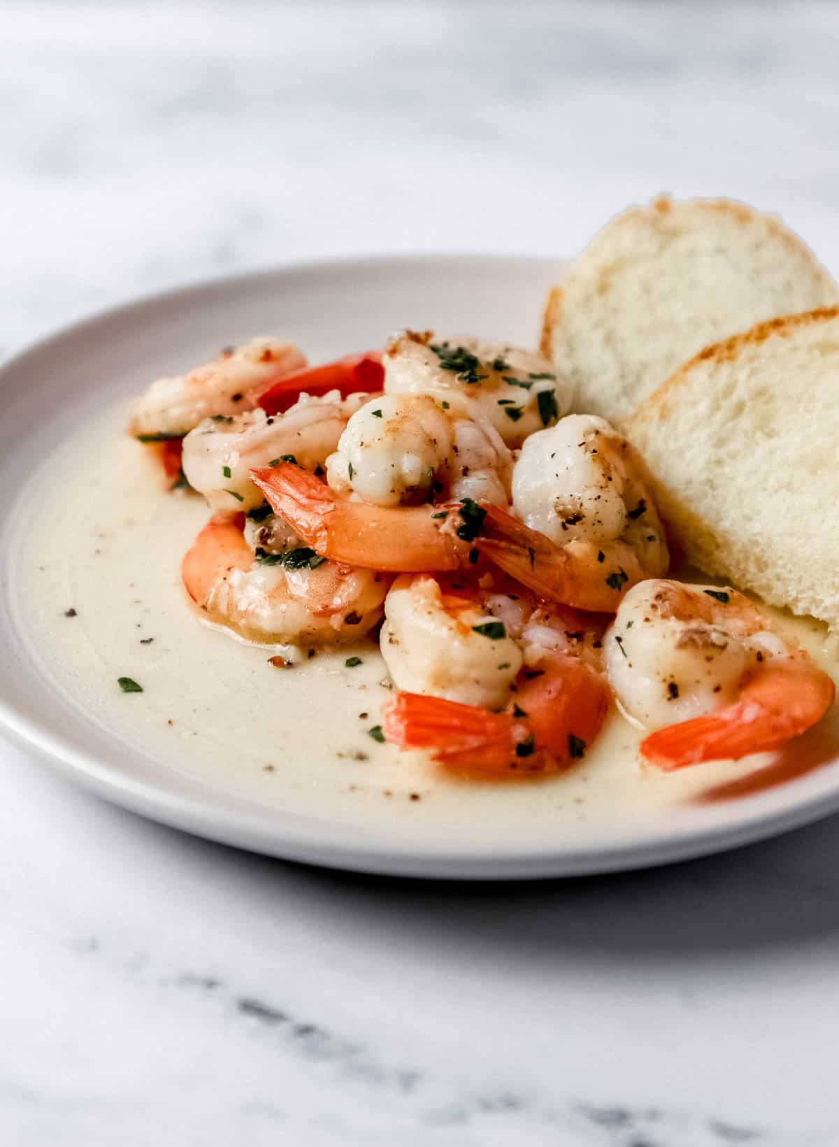 Close up side view of serving of finished shrimp on small white plate with piece of bread. 