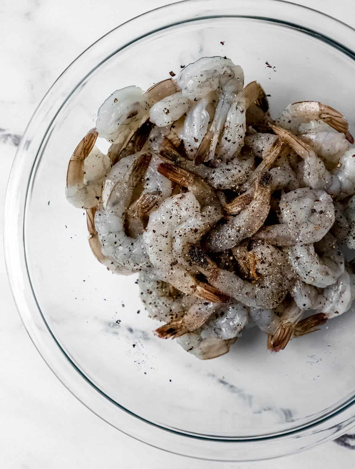 Raw shrimp, salt, and black pepper in glass mixing bowl. 