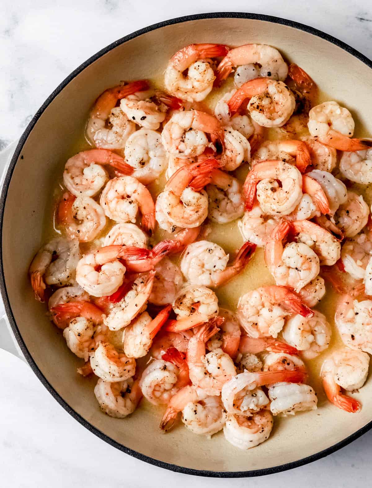 Overhead view of braiser pan with shrimp, butter, and minced garlic in it. 