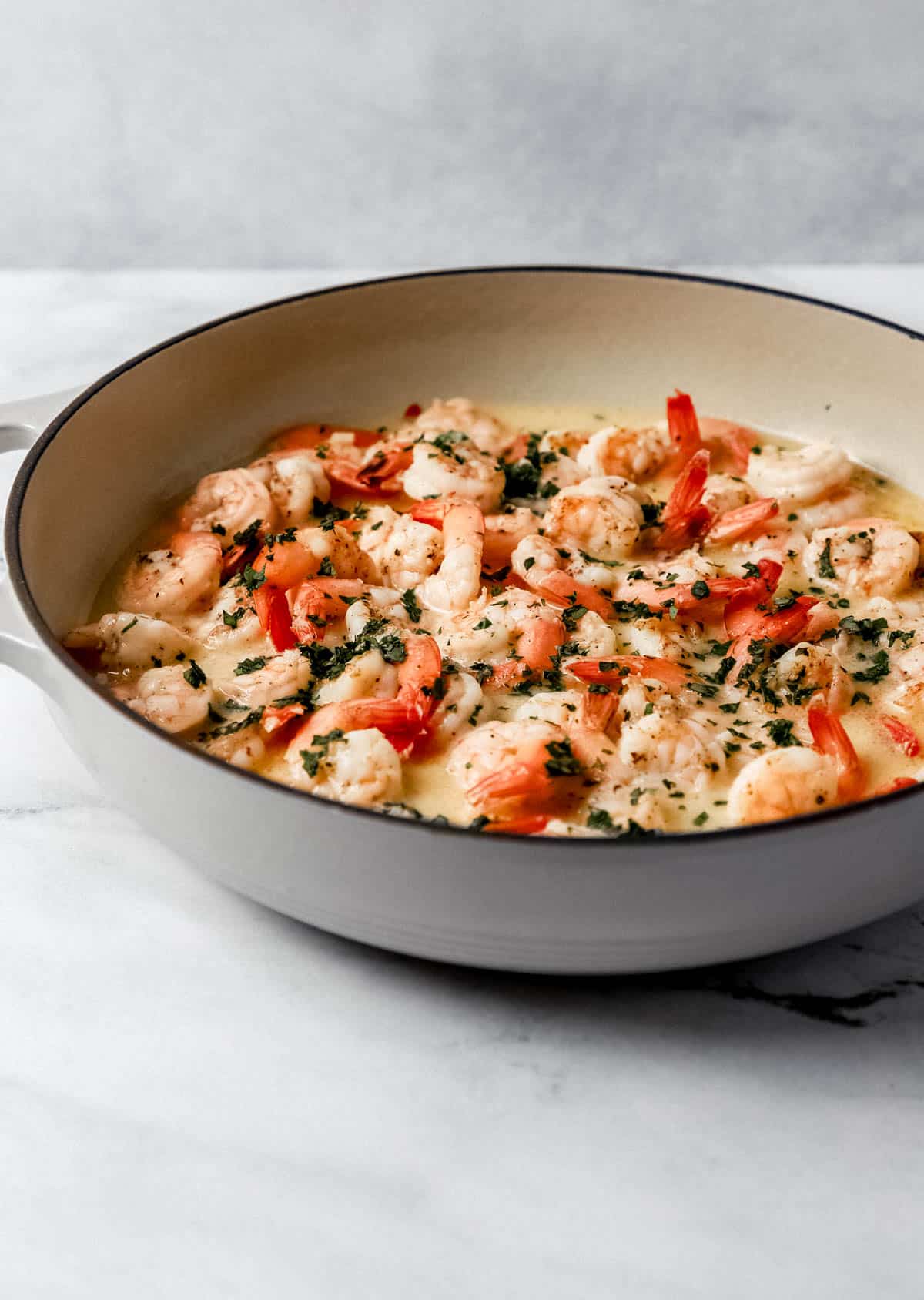 Close up side view of finished shrimp in pan topped with fresh chopped parsley. 