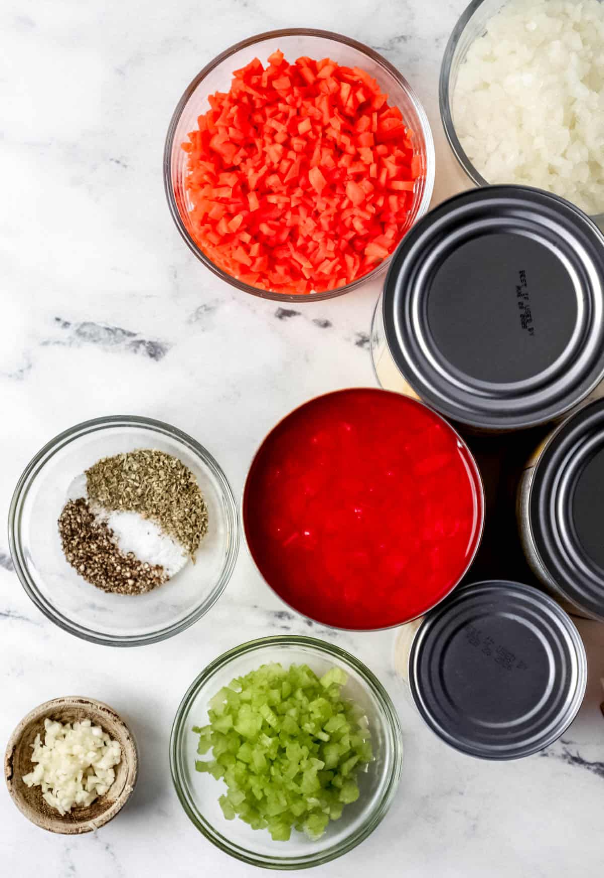 Overhead view of ingredients needed to make tomato soup in separate containers on marble surface. 