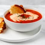 Close up side view of bowl of soup with piece of grilled cheese in it.