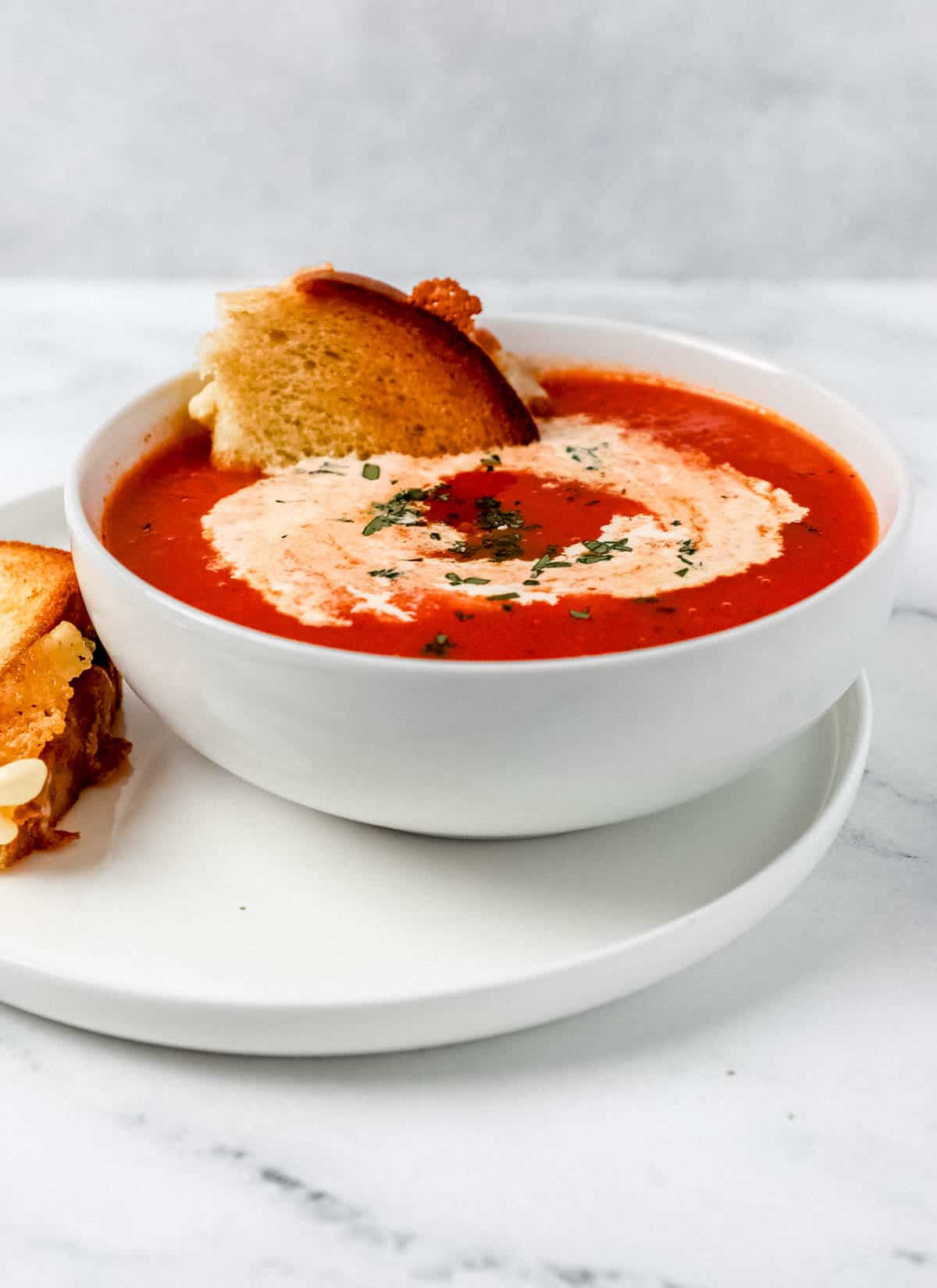 Close up side view of bowl of soup with a piece of grilled cheese in it. 