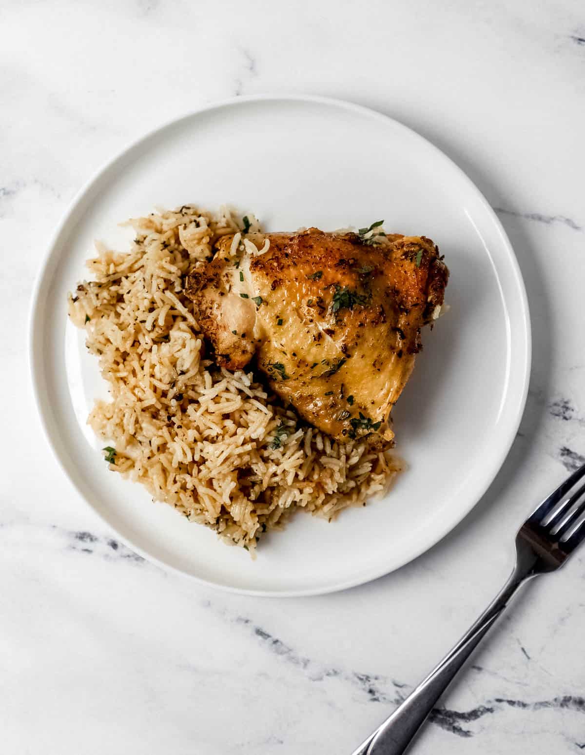 Single serving of chicken and rice on white plate beside a fork on marble surface. 