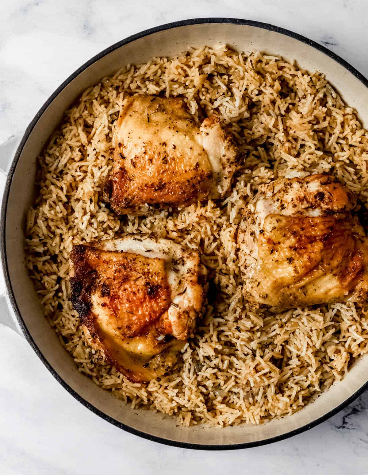 Overhead view of finished chicken and rice in braiser pan on marble surface. 