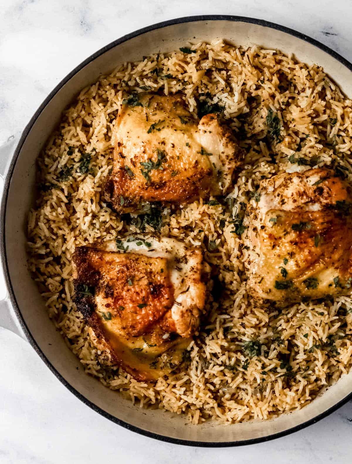 Overhead view of chicken and rice in braiser pan topped with chopped parsley. 