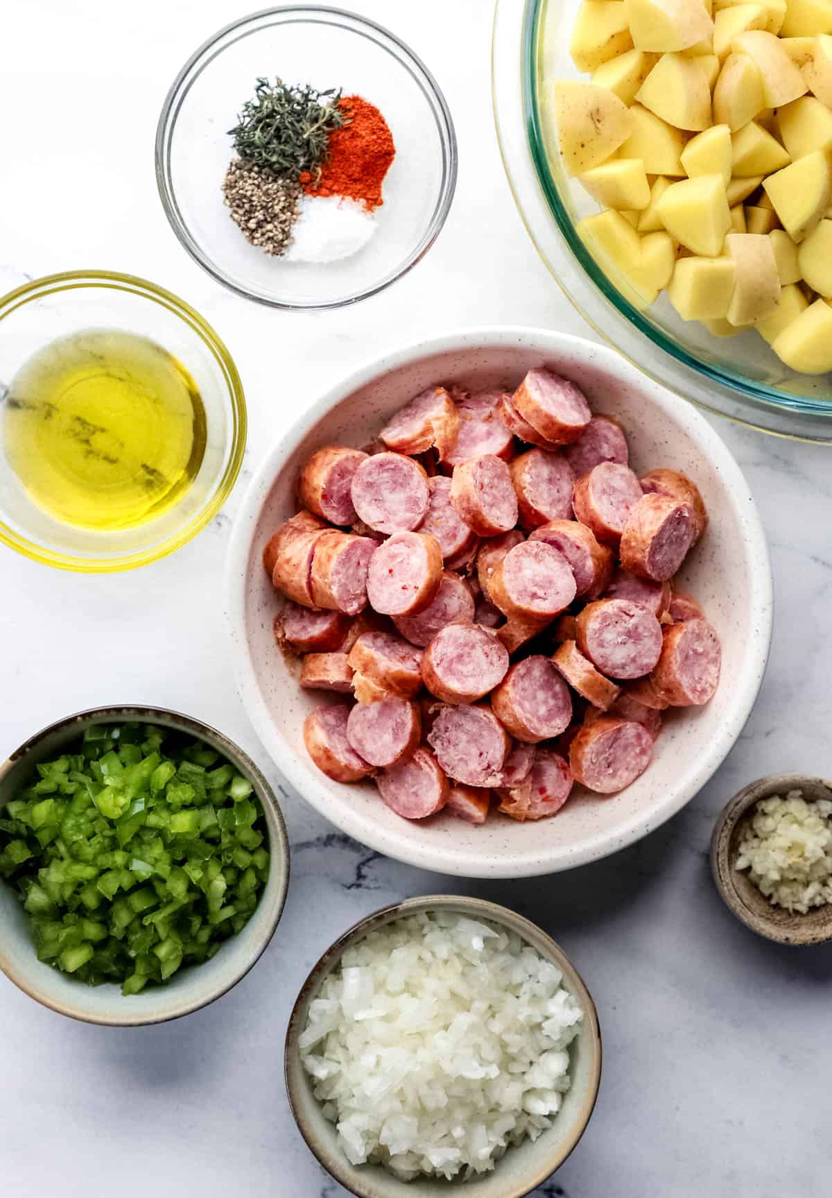 Overhead view of ingredients needed to make sausage and potatoes in separate bowls. 