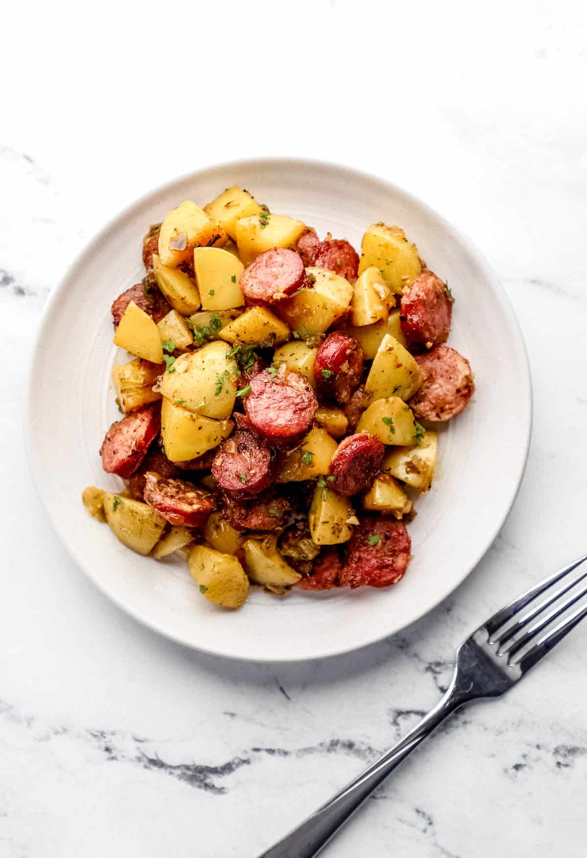 Overhead view of serving of sausage and potatoes on white plate beside a fork. 