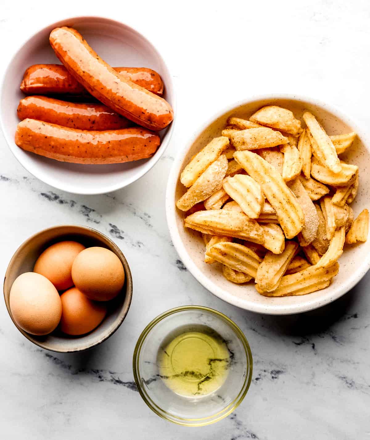 Ingredients needed to make sheet pan breakfast in separate bowls on marble surface. 