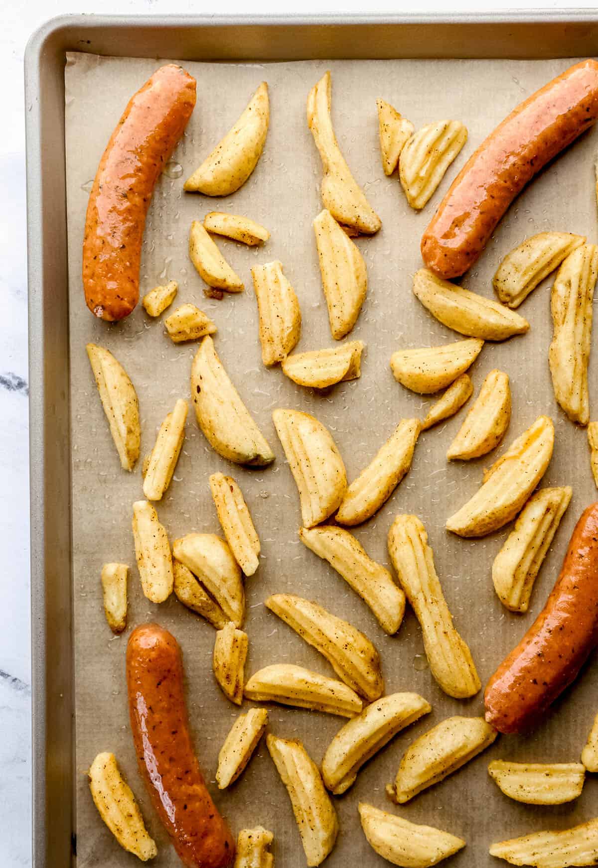 Potato wedges and sausage tossed in olive oil on parchment lined baking sheet. 