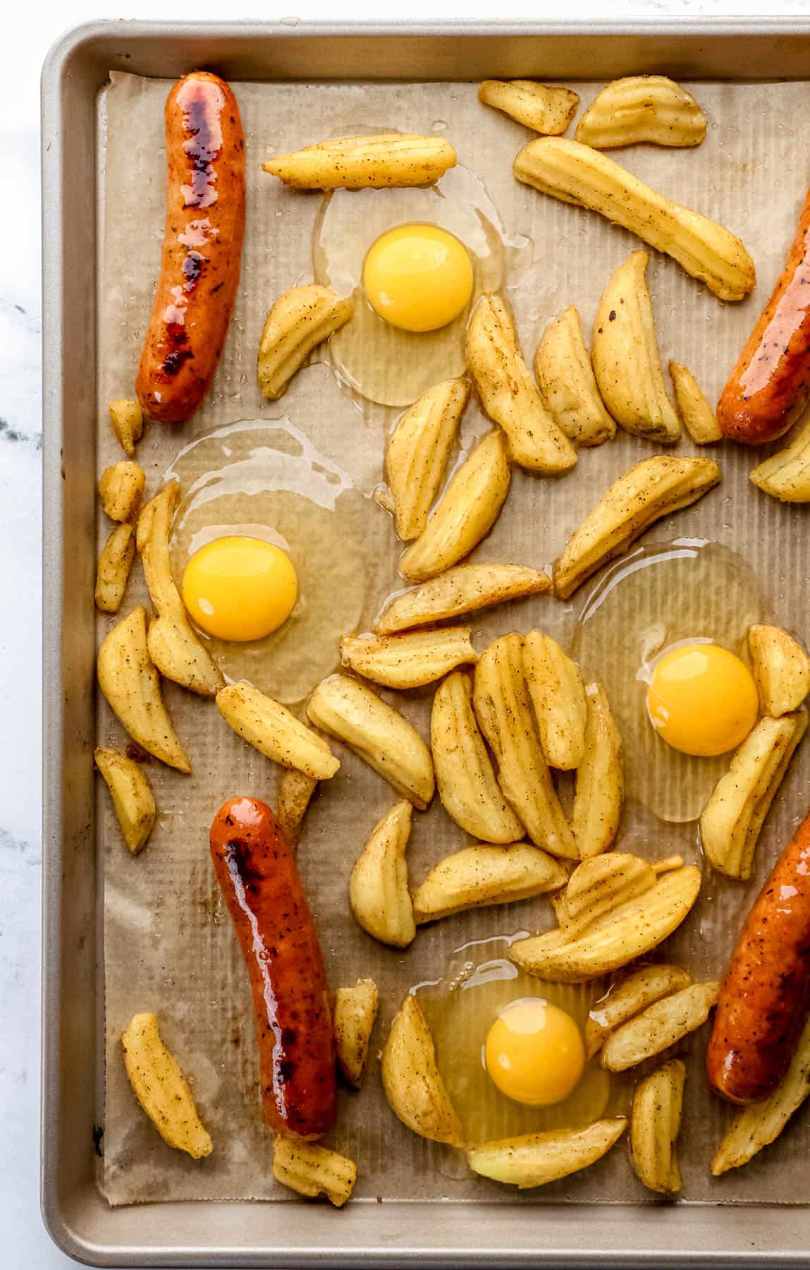 Raw eggs added to parchment lined baking sheet with potatoes and sausage. 