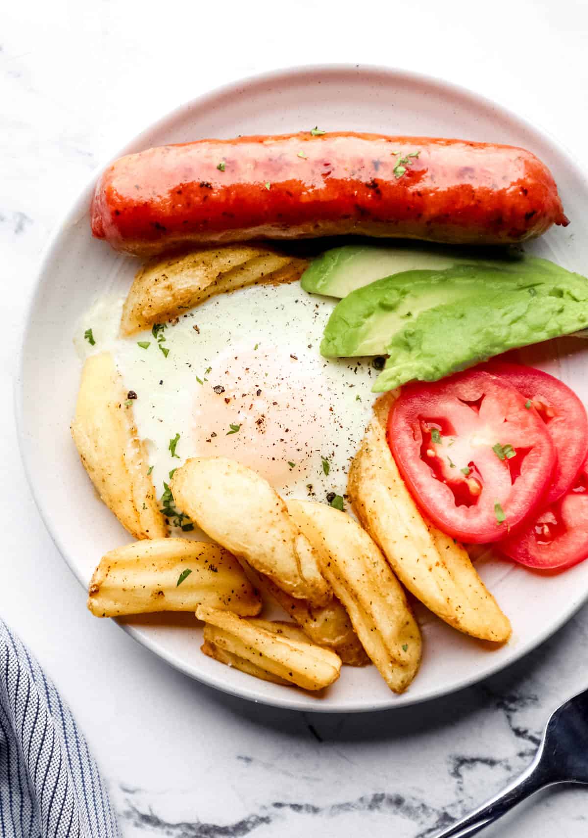 Overhead view of white plate with breakfast on it beside a cloth napkin and fork. 