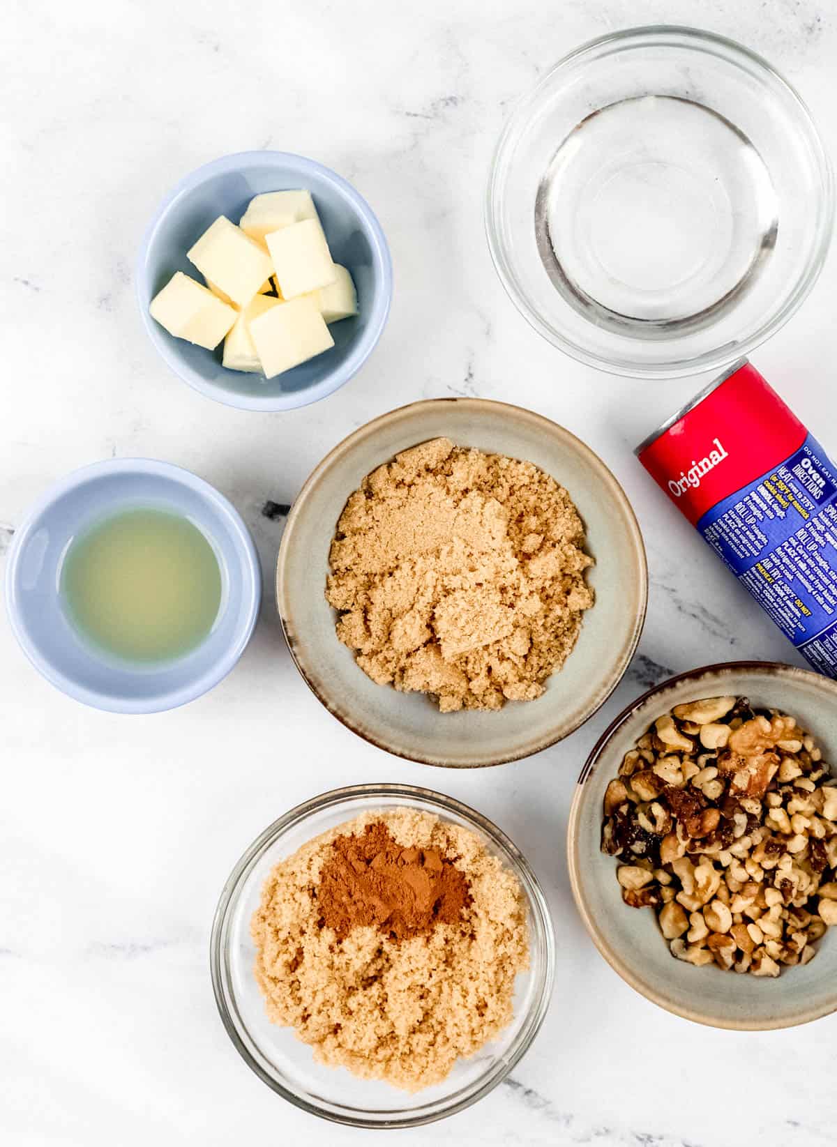 Overhead view of ingredients needed to make sticky buns in separate bowls on marble surface. 