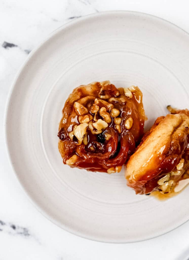 Overhead view of two sticky buns on white plate on marble surface.