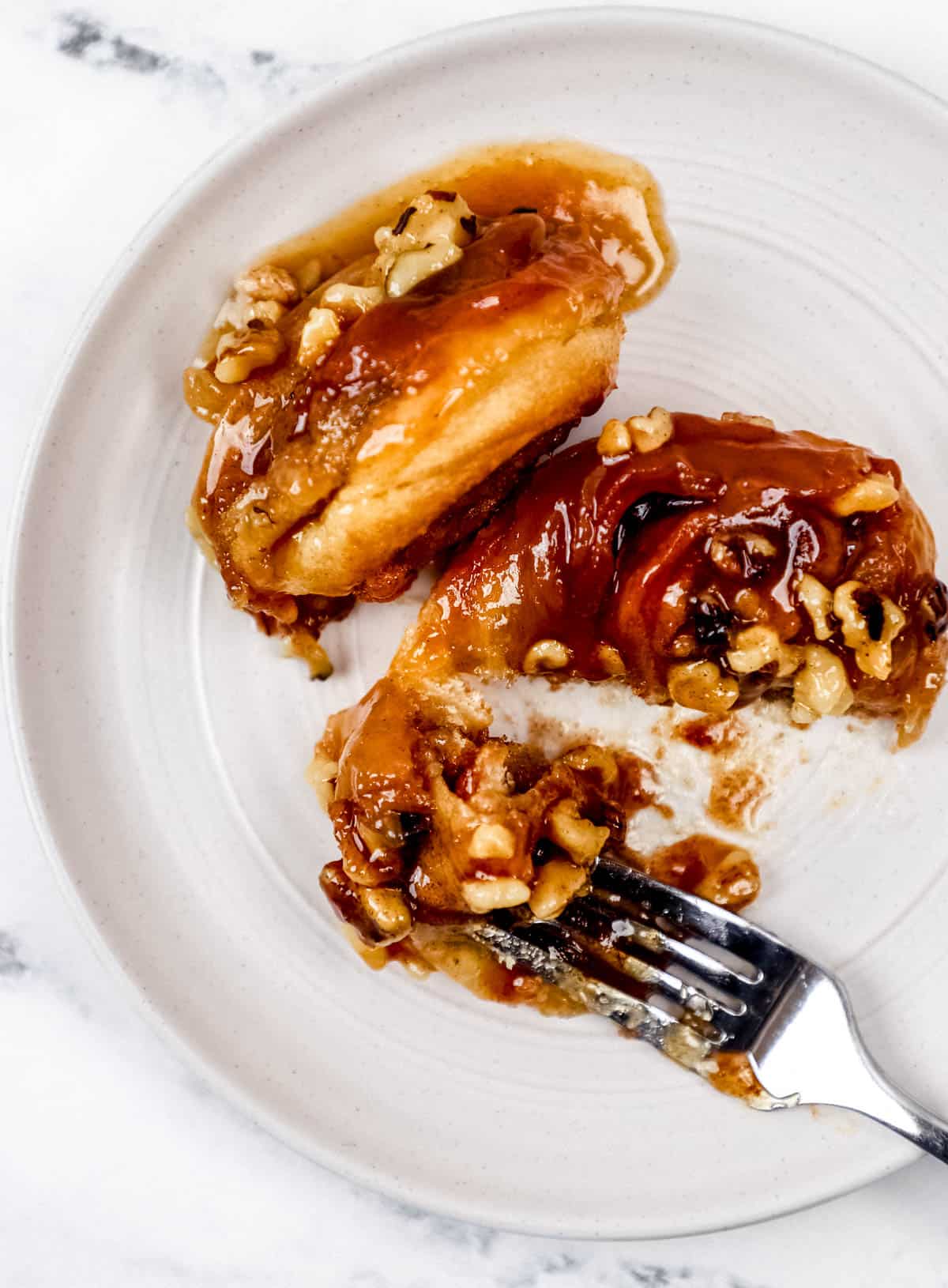 Two sticky buns on white plate with fork in it. 