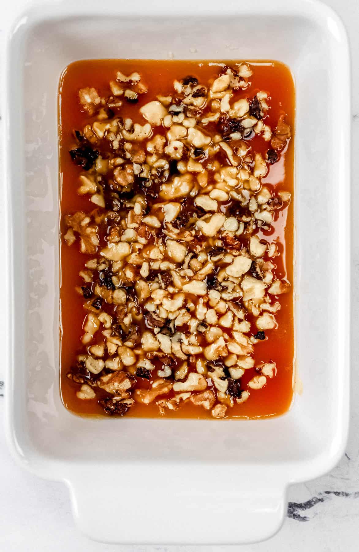 Sticky mixture and chopped walnuts added to bottom of baking dish. 