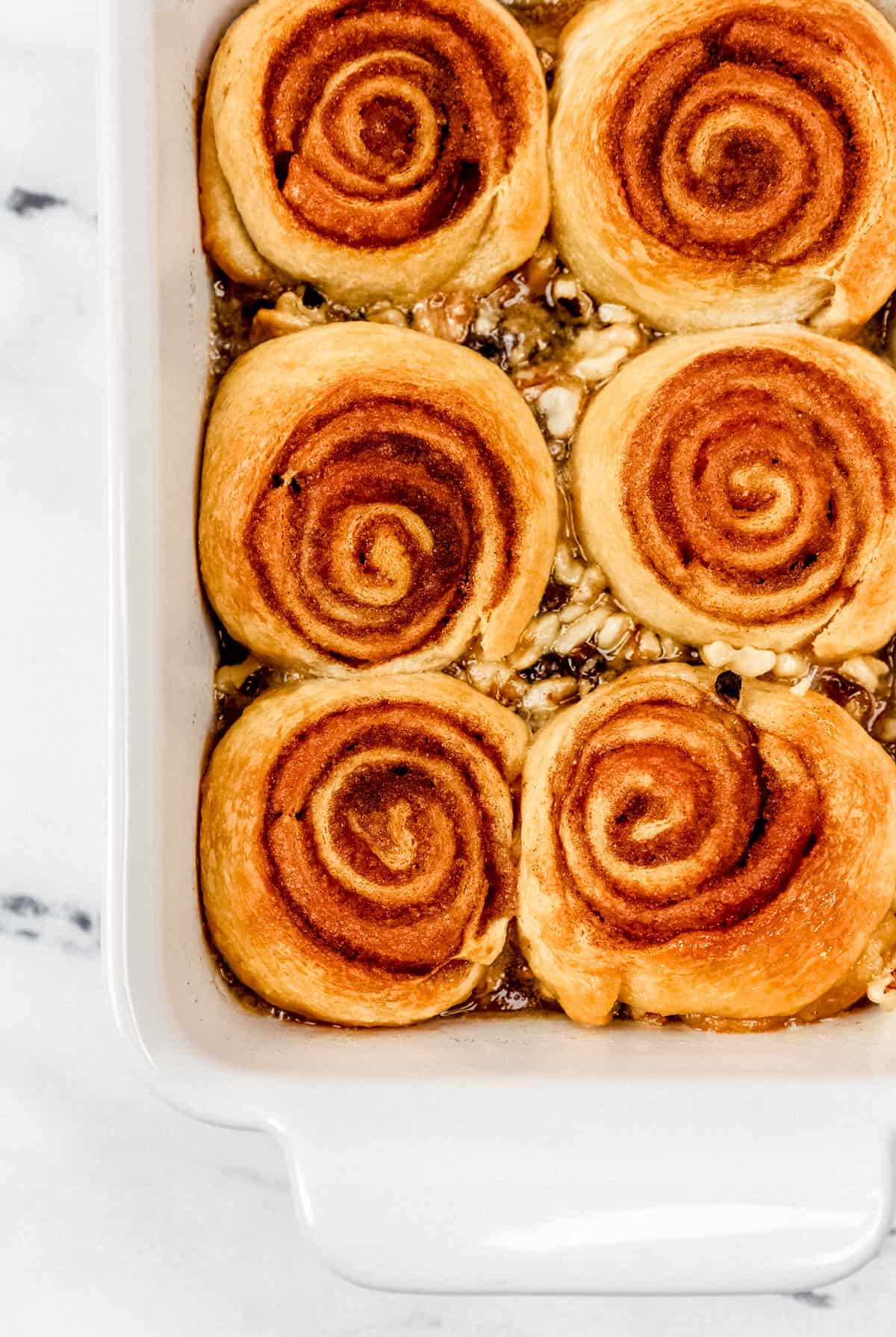 Overhead view of finished sticky buns in a baking dish on marble surface. 