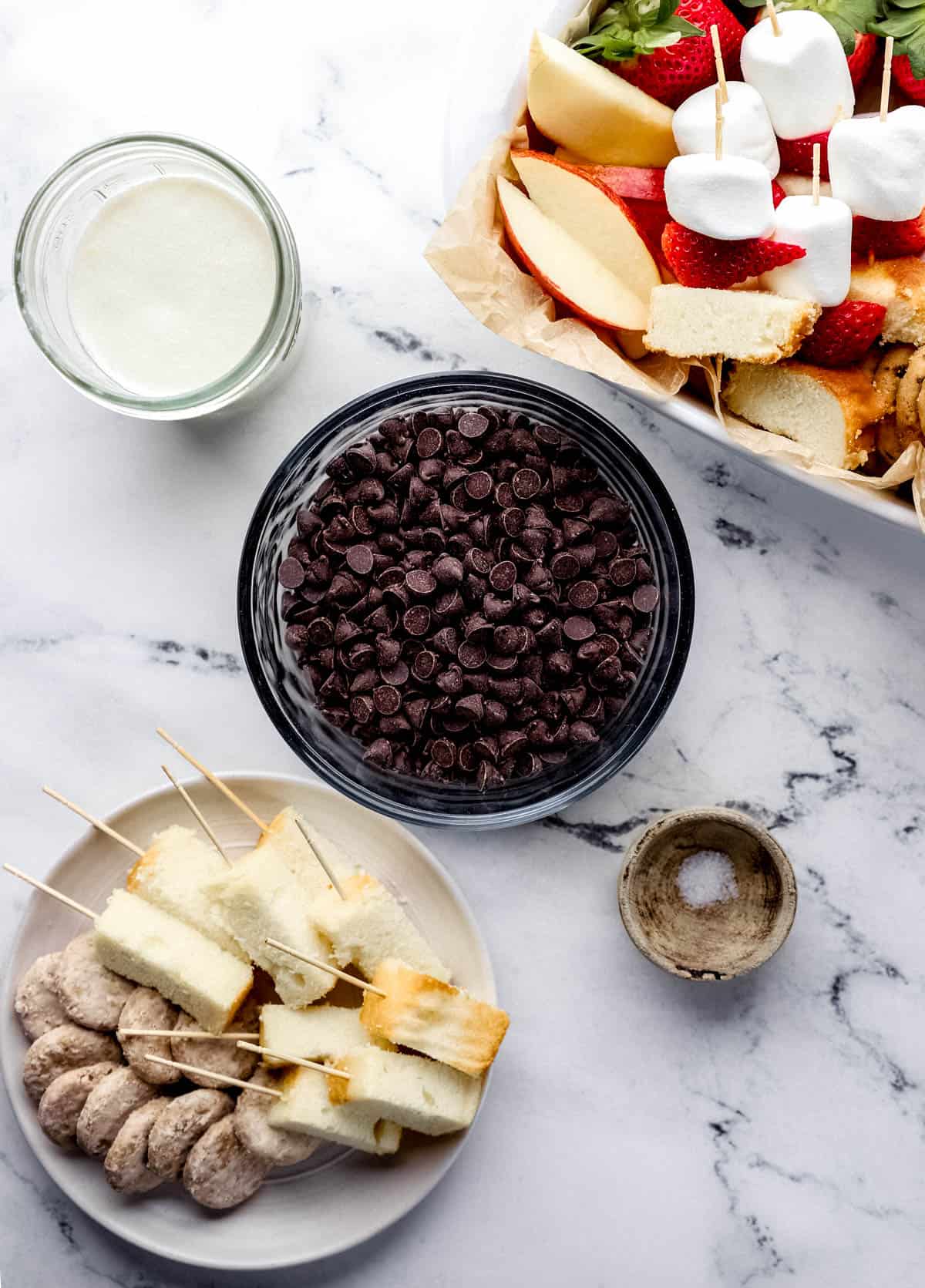 Overhead view of ingredients needed to make chocolate fondue in separate bowls on marble surface. 