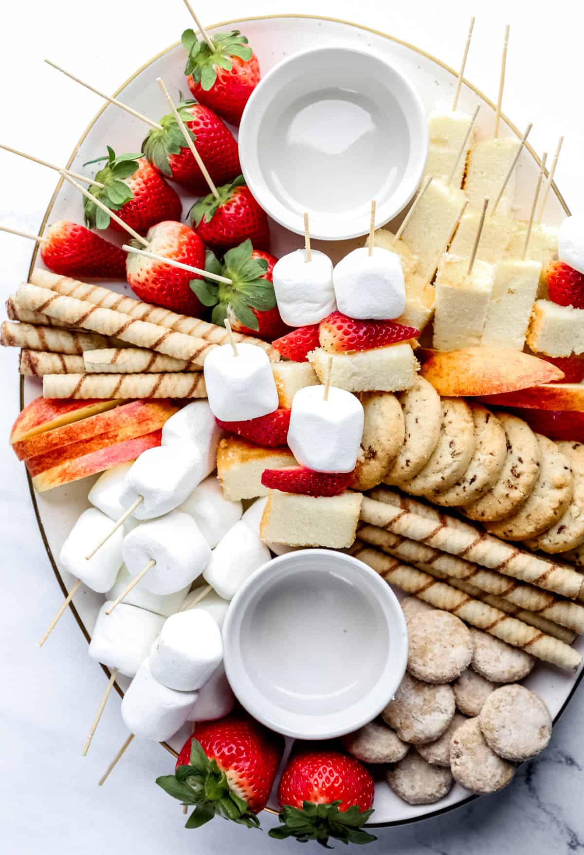 Large white tray with treats to dip in chocolate fondue and two empty small white bowls.