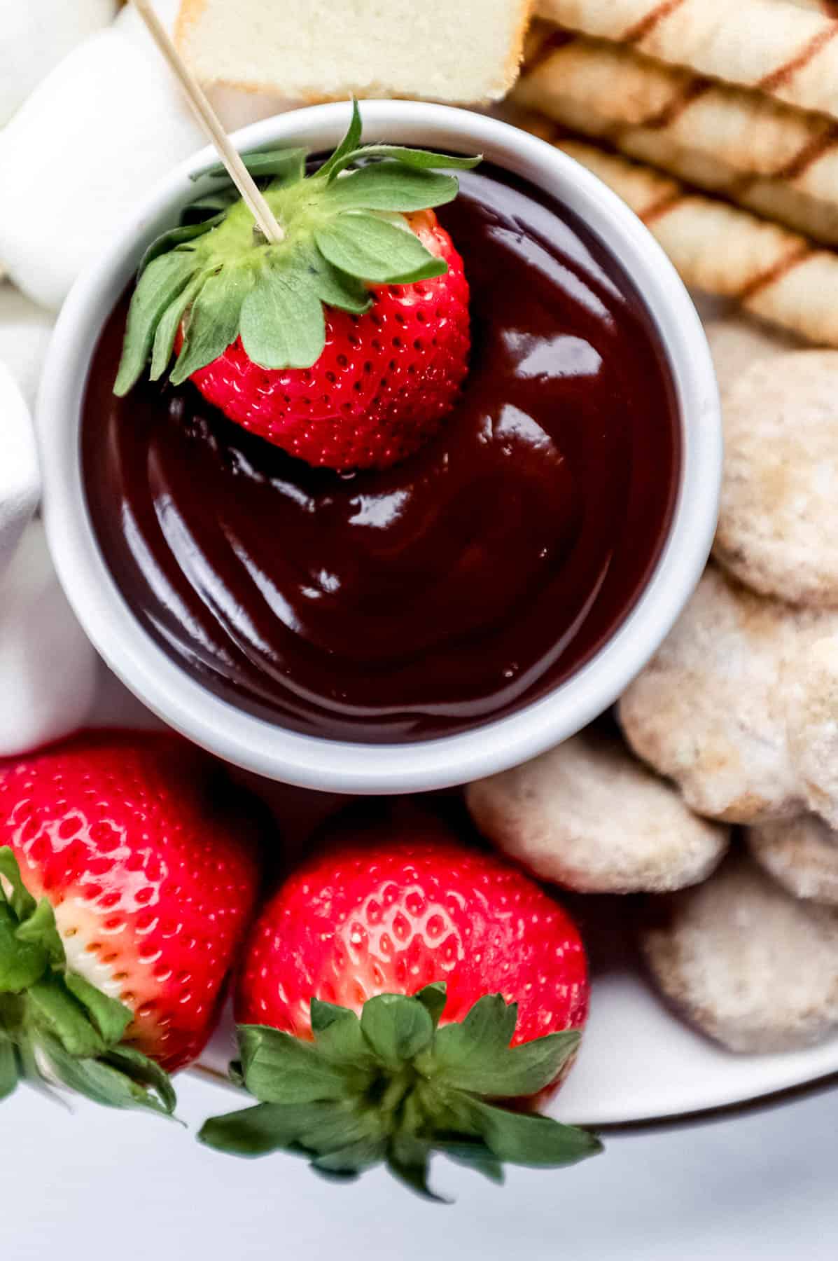 Close up view of chocolate fondue in white bowl with a strawberry in it on top of dessert board.