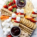 Overhead view of white dessert board with chocolate fondue dippers on it on top of marble surface.