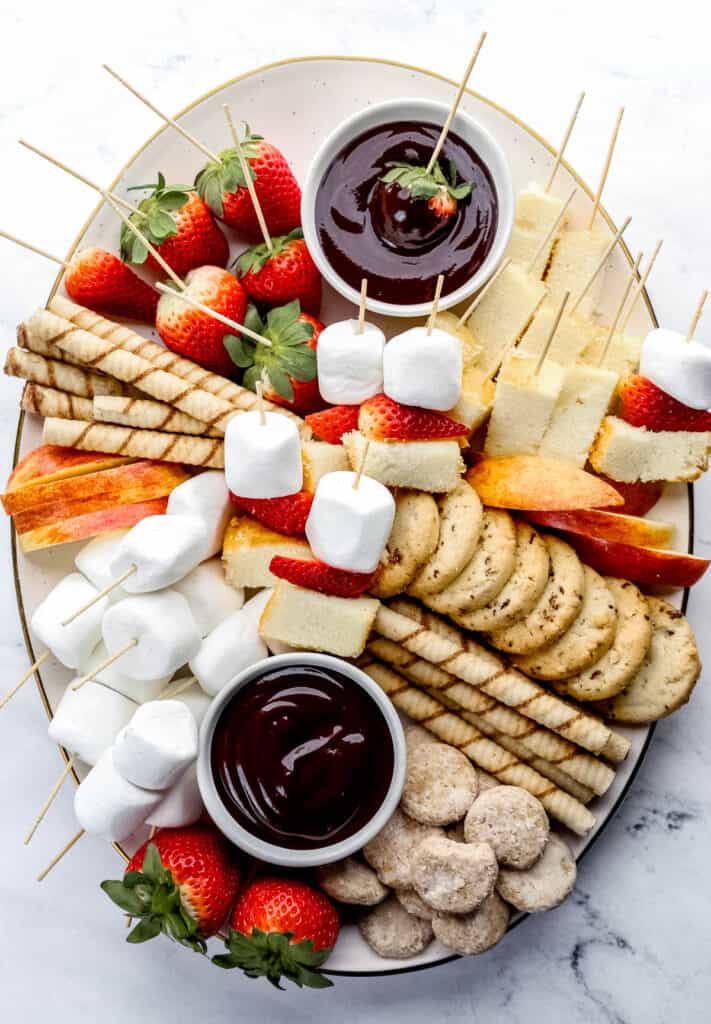 Overhead view of white dessert board with chocolate fondue dippers on it on top of marble surface.