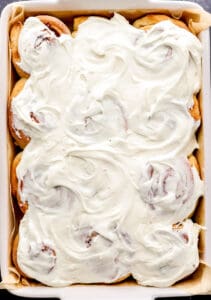 Overhead view of cinnamon rolls topped with frosting in parchment lined baking dish.