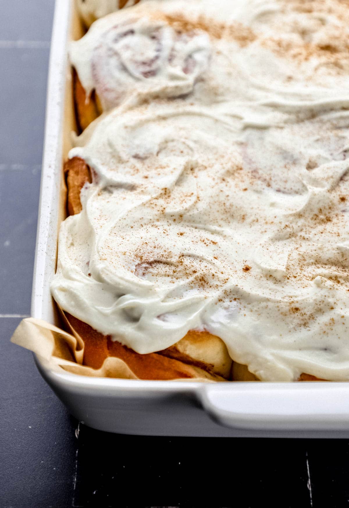 Close up front view of baked cinnamon rolls topped with frosting and ground cinnamon. 