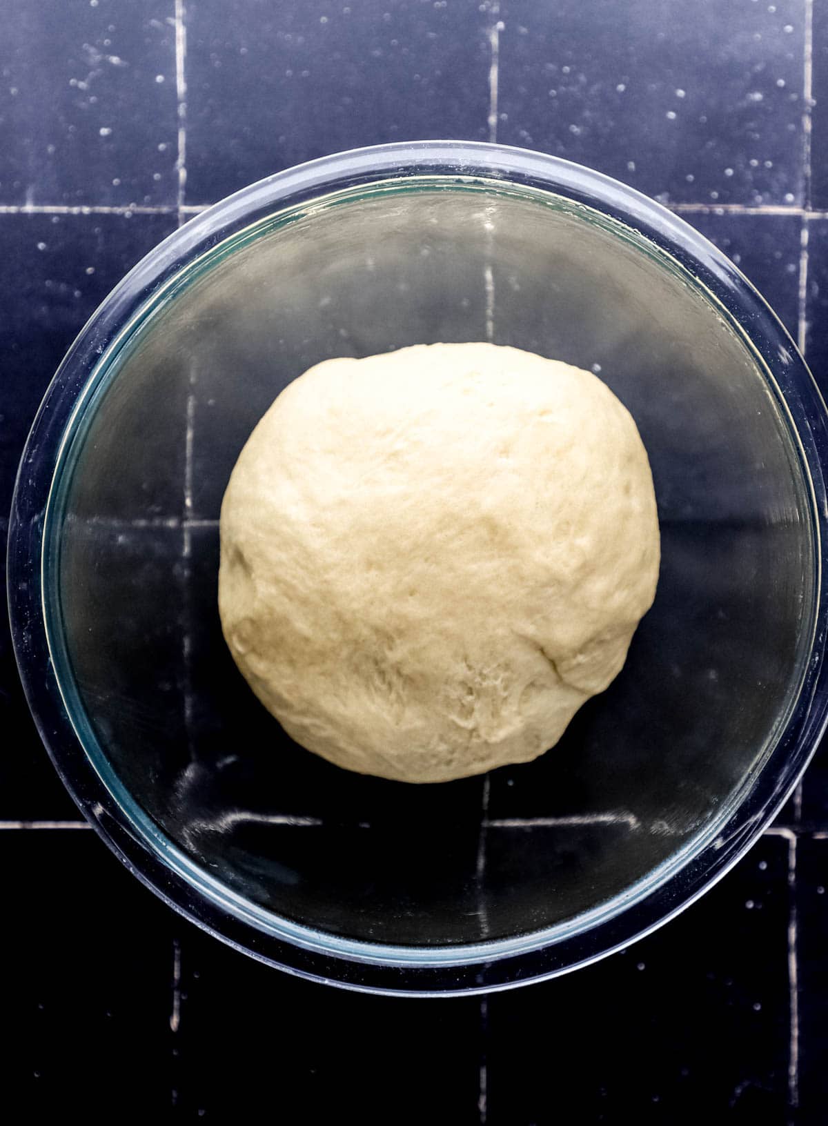 Overhead view of dough in large glass bowl before rising. 