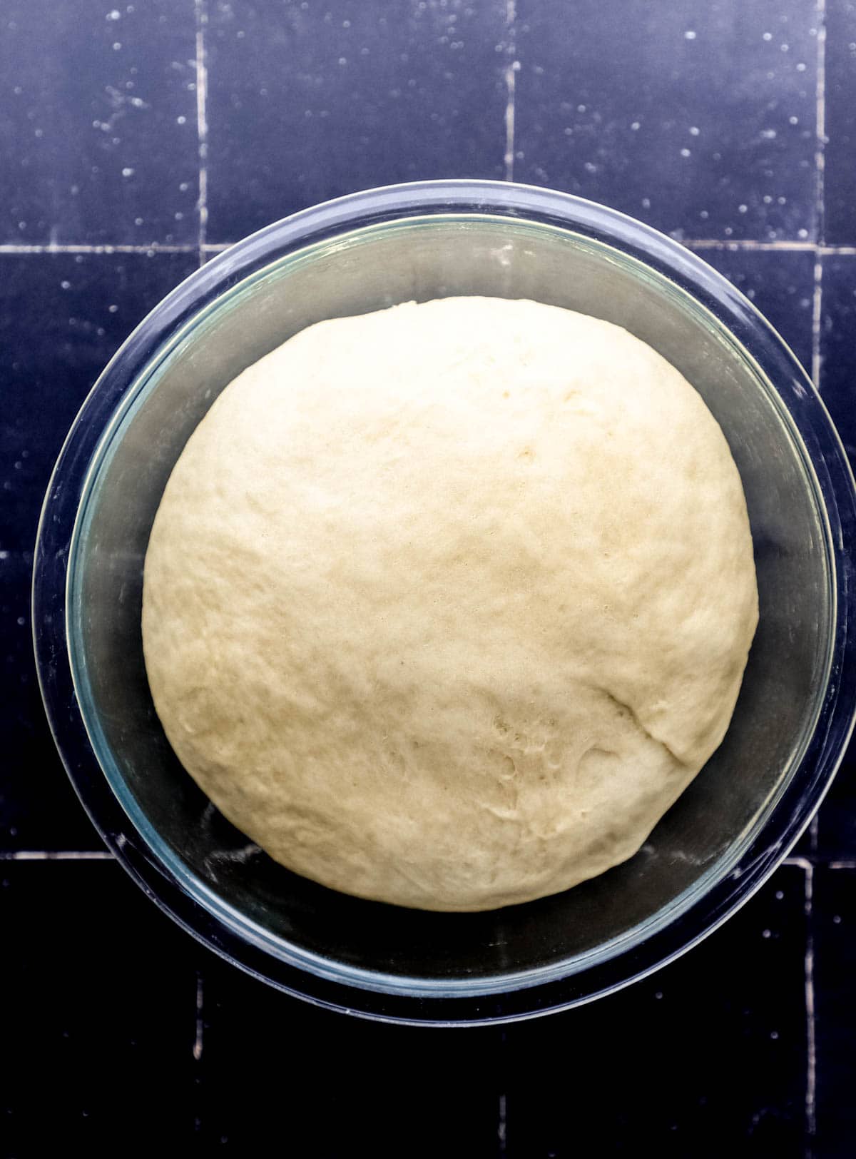 Overhead view of dough in large glass bowl after rising. 