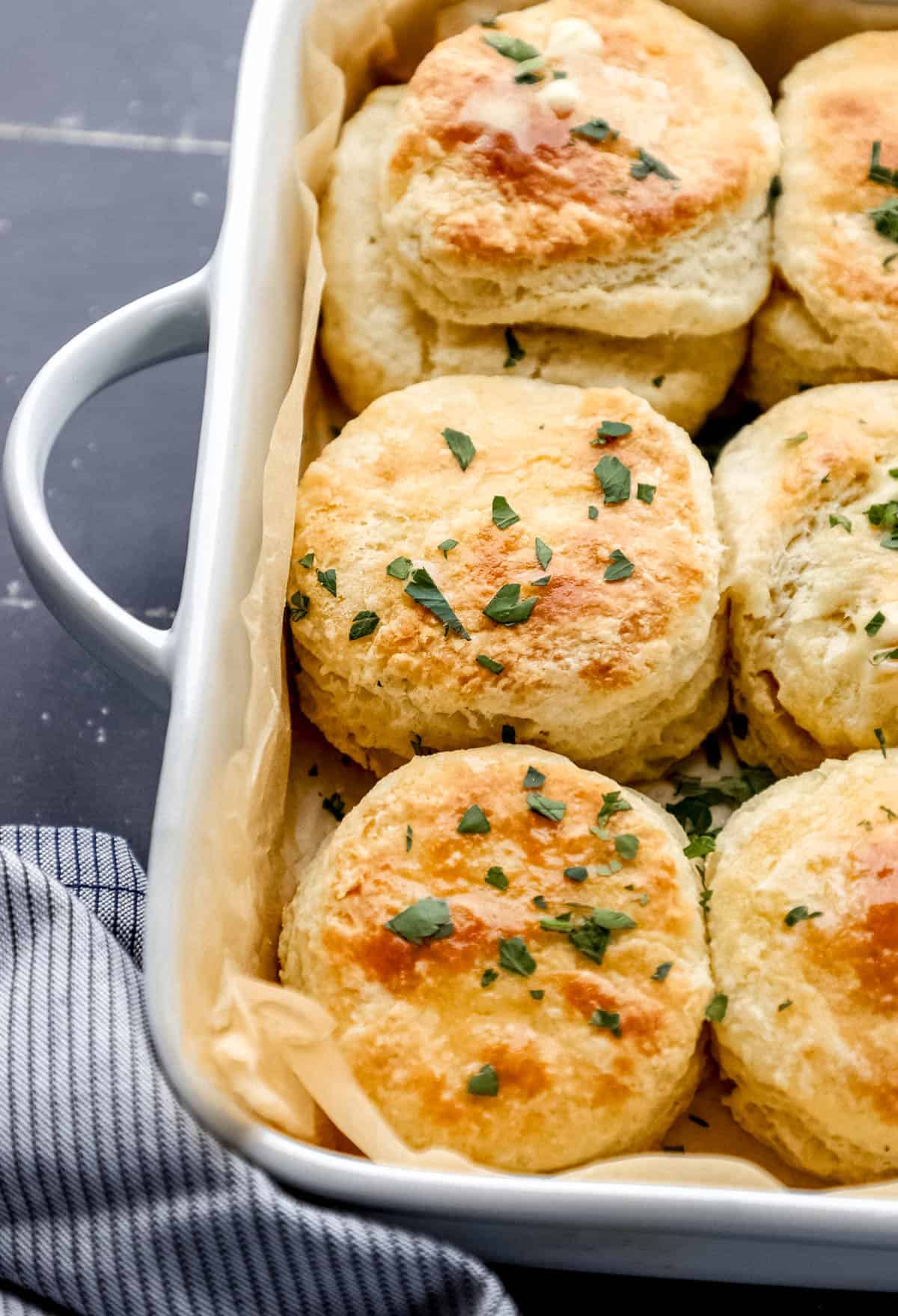 Close up view of baked biscuits in white baking dish beside a cloth napkin on black surface. 