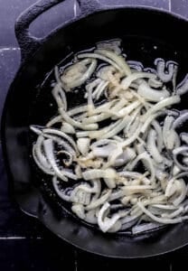 Overhead view of sliced onion cooking in oil.