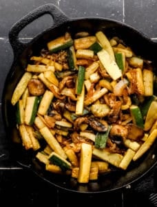 Hibachi vegetables in cast iron skillet on black tile surface.