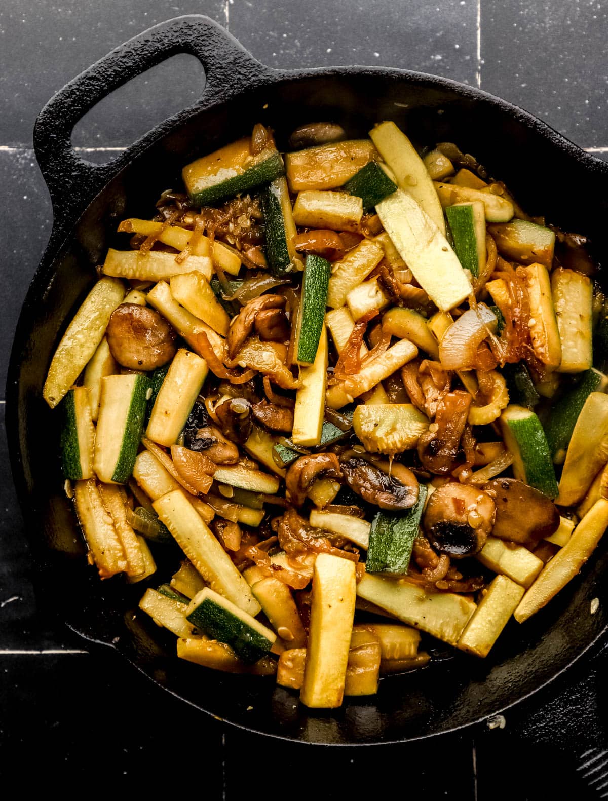 Cooked vegetables in large cast iron skillet on black tile surface. 