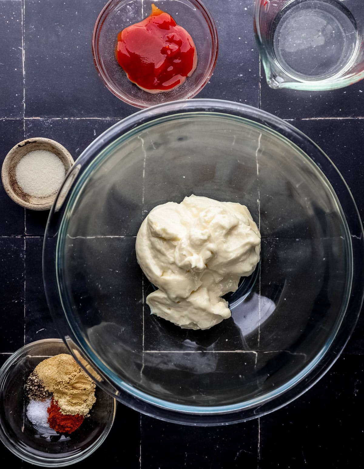 Overhead view of ingredients needed to make sauce in separate bowls on black tile surface. 