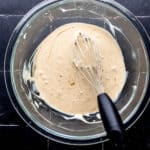 Overhead view of sauce ingredients combined in glass mixing bowl with whisk in it.