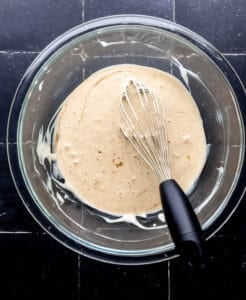 Overhead view of sauce ingredients combined in glass mixing bowl with whisk in it.